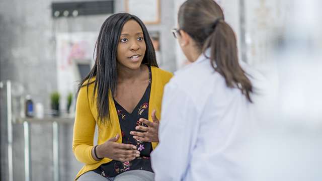 A black female patient talking with a white female doctor.